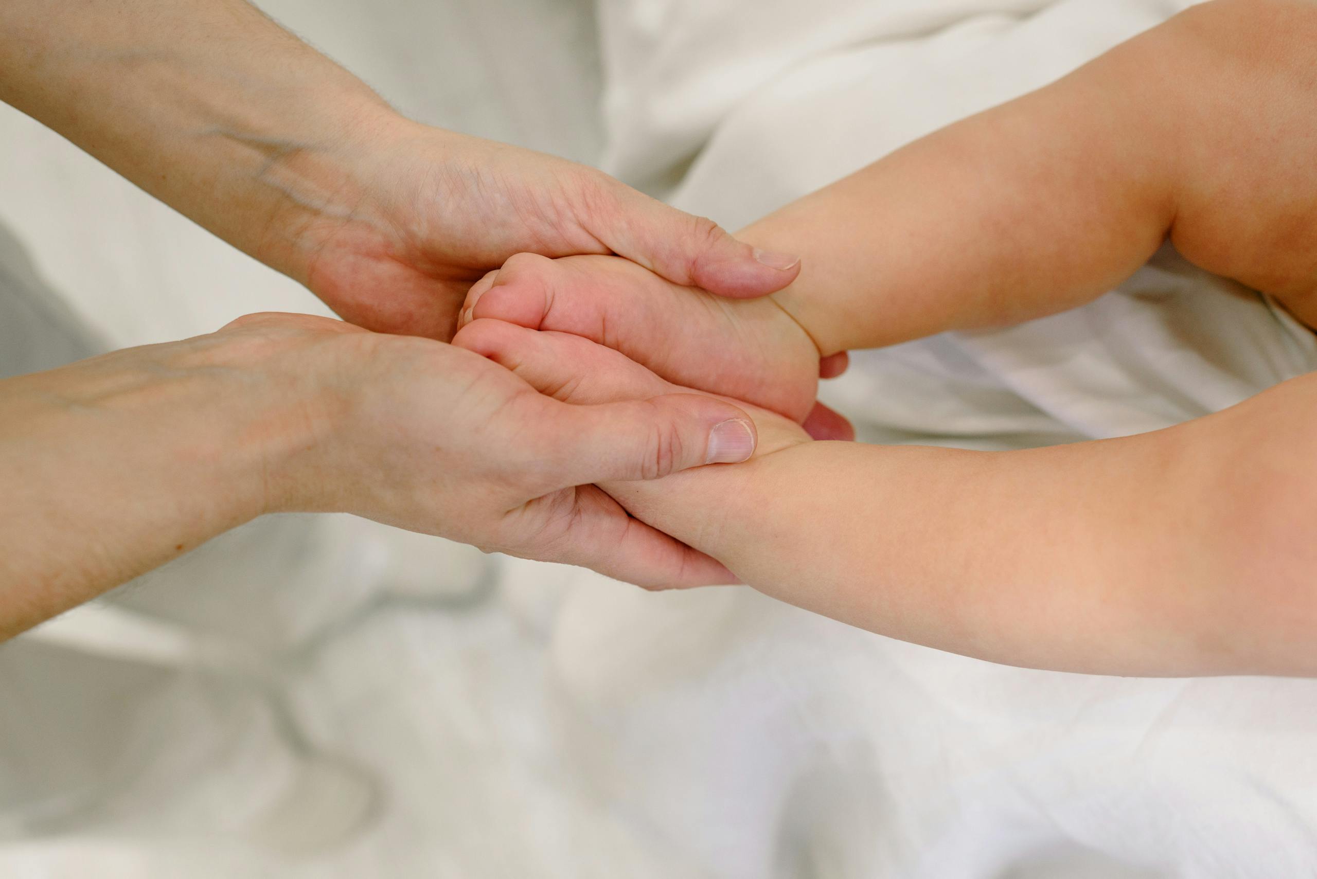 Adult gently massaging infant's hands, promoting bonding and relaxation, captured in a warm setting.