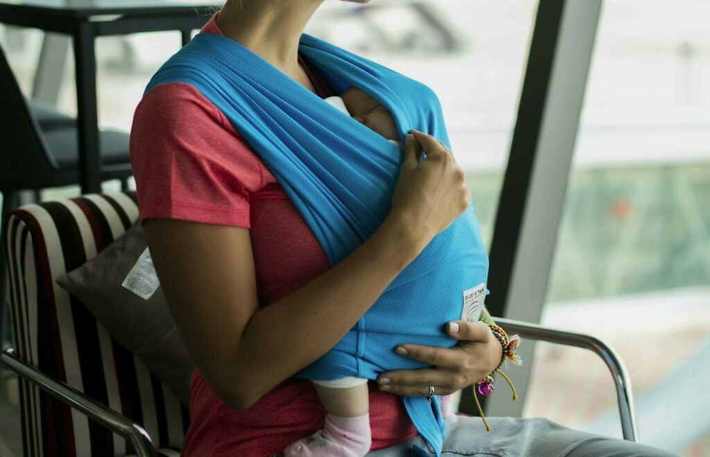 Photo par Juliia Abramova A mother with her baby in a sling looks out the window at Phuket airport.